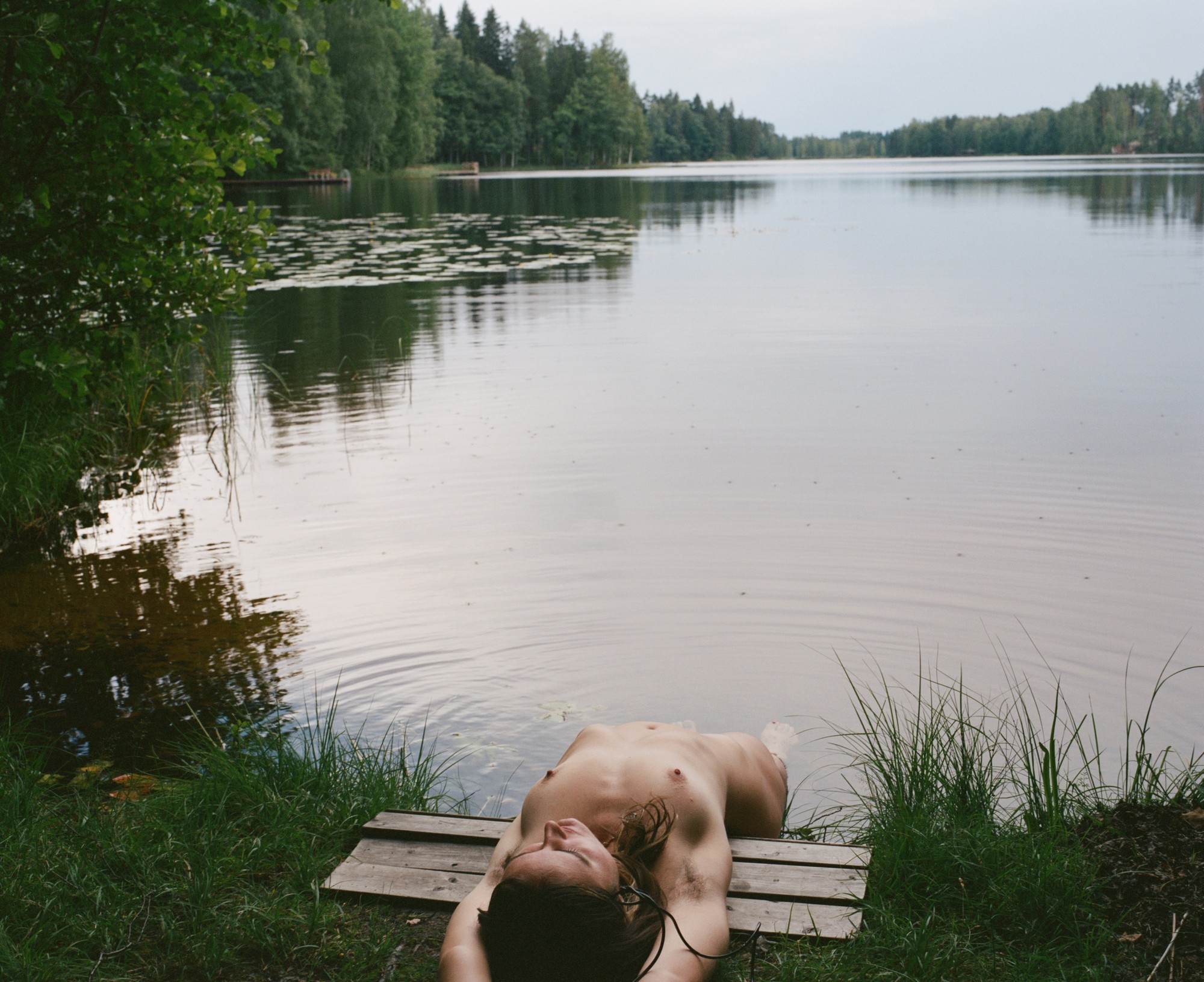 Figure lying on a wooden dock by a lake
