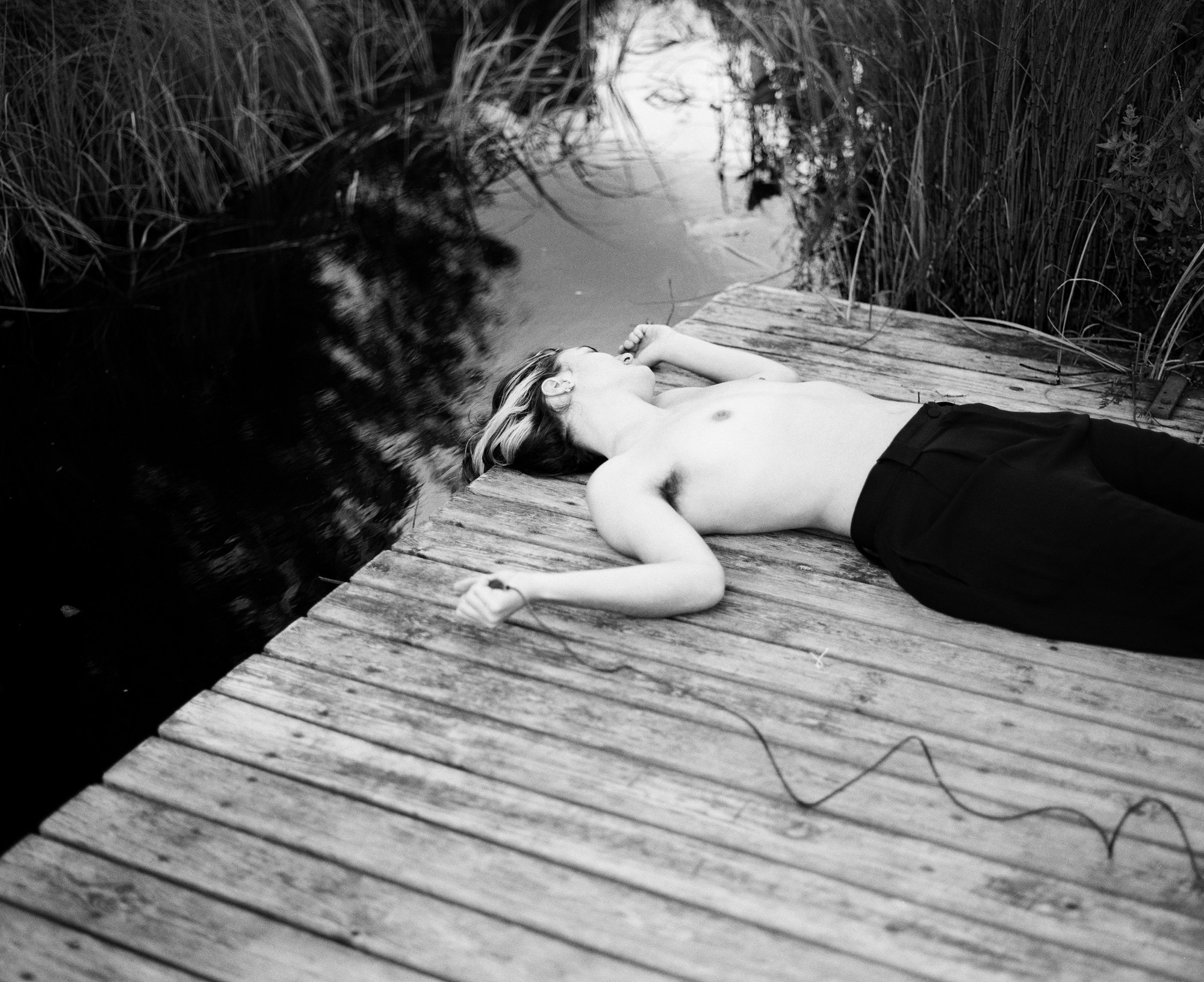 Figure lying on a wooden jetty among reeds