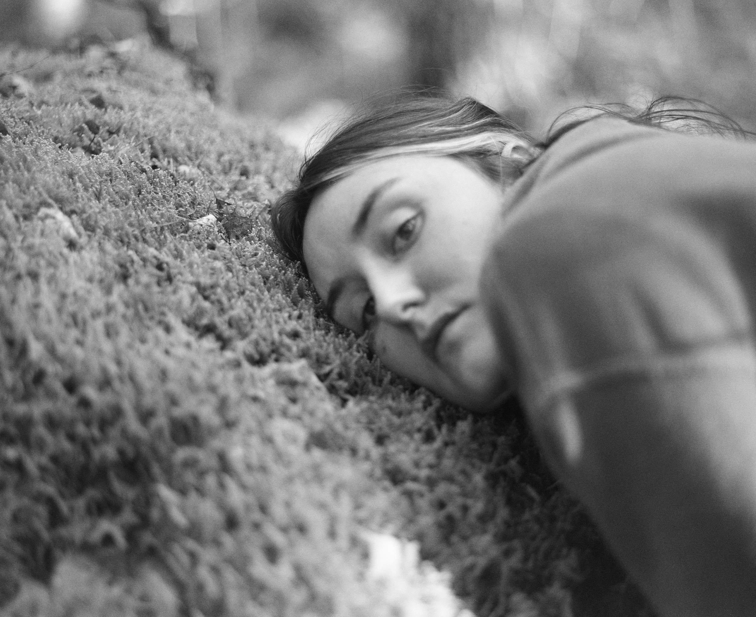 Close-up of a figure lying with their head on a mossy log, looking at the camera