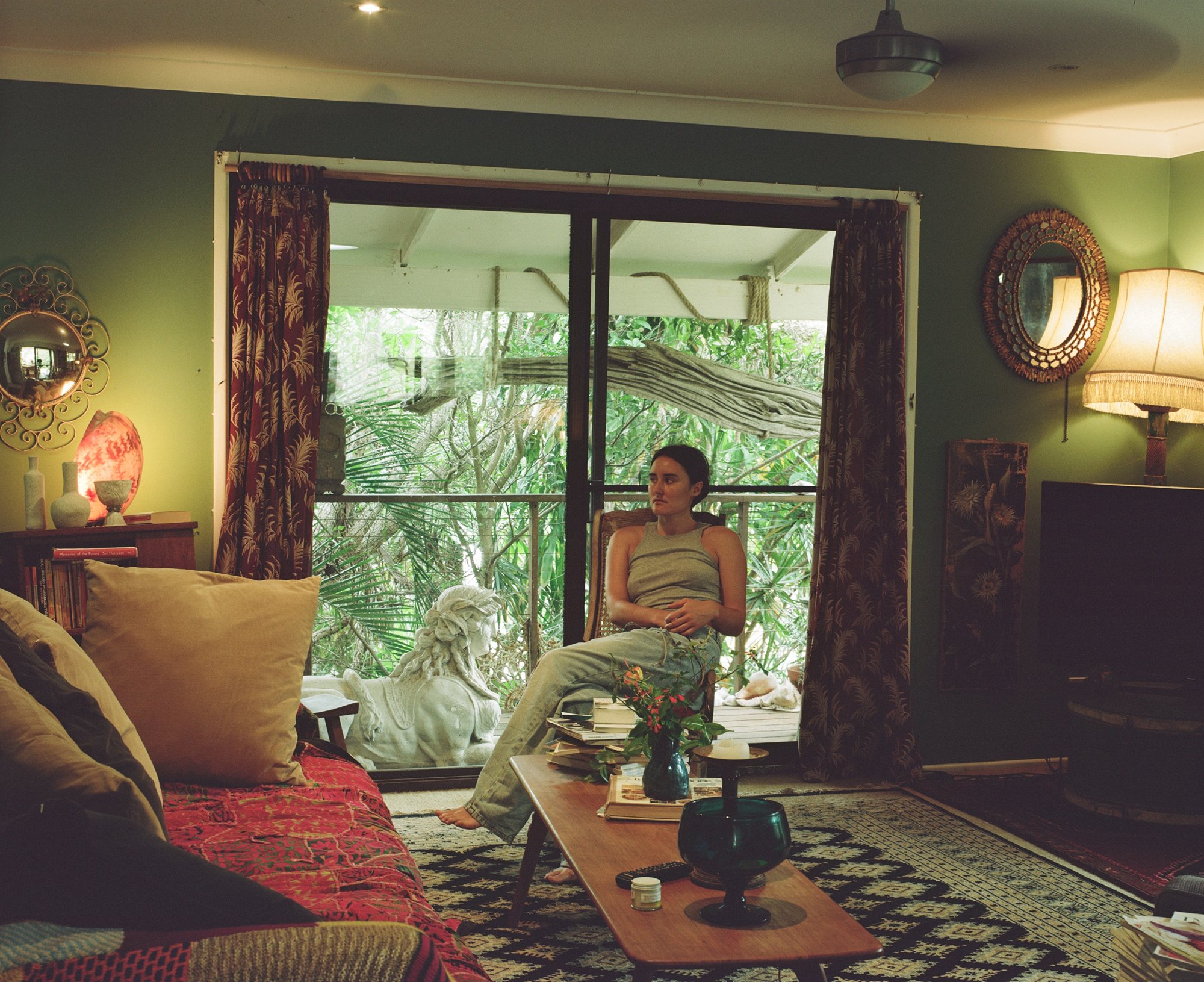 Woman sitting in an armchair by open doors leading to a jungle-like garden