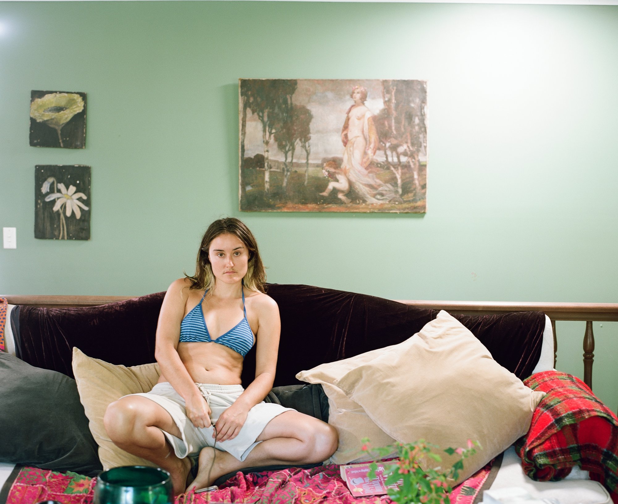 Woman in a striped bikini top sitting on a velvet sofa beneath a painting