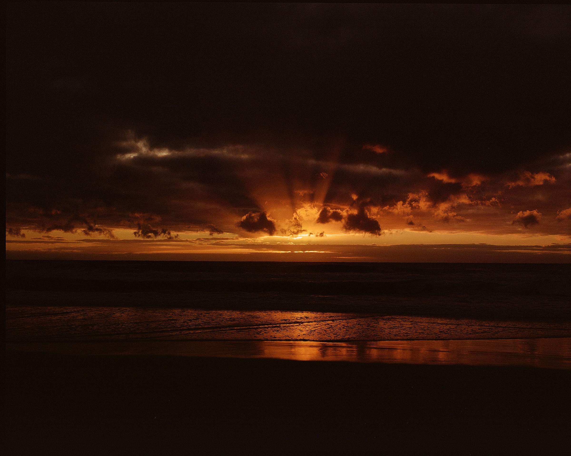 Dark sunset over the ocean, sun breaking through clouds