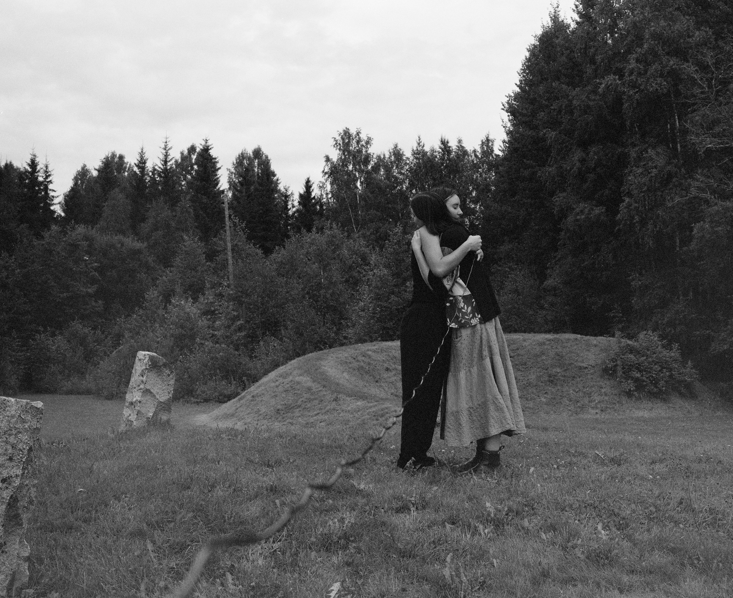Black and white photograph of two figures embracing in a field with standing stones