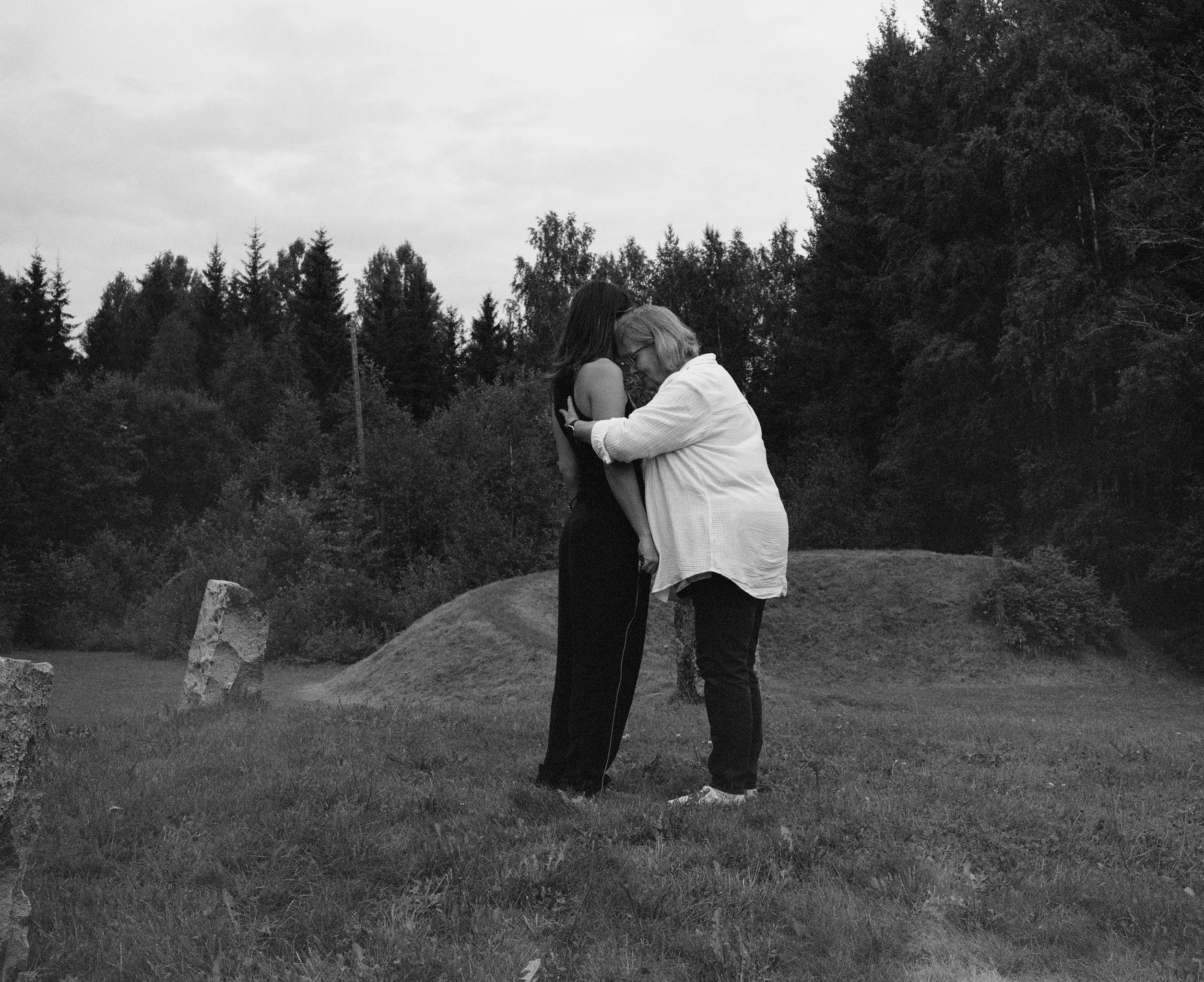 Black and white photograph of two figures embracing in a field with standing stones