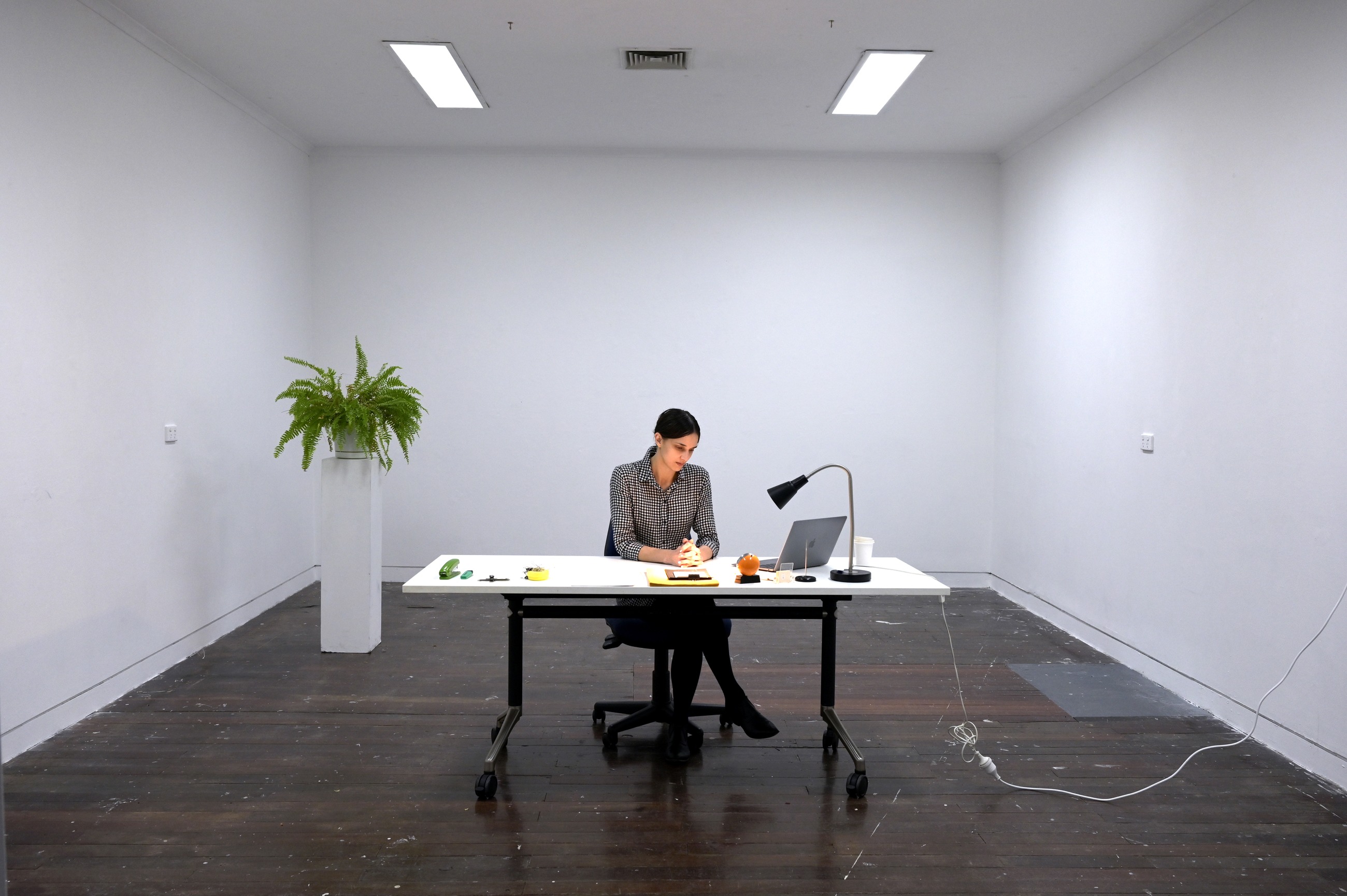 Performance in a white gallery room, a figure seated at a desk