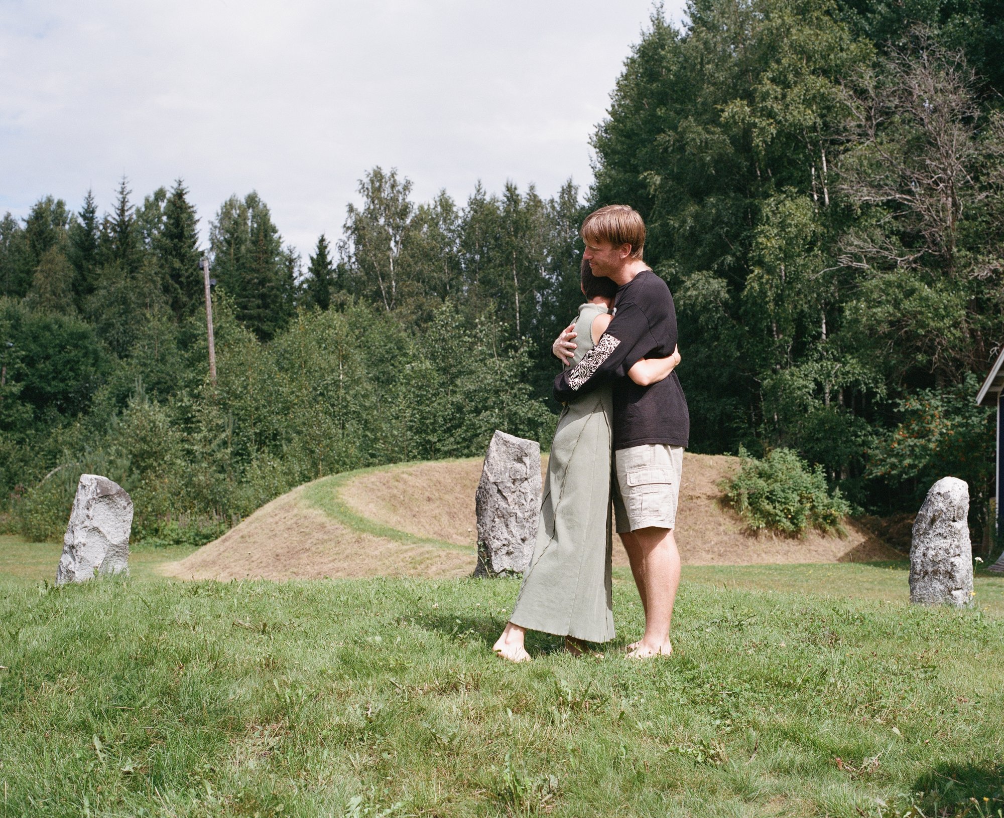 Two figures embracing among standing stones, a red barn behind them