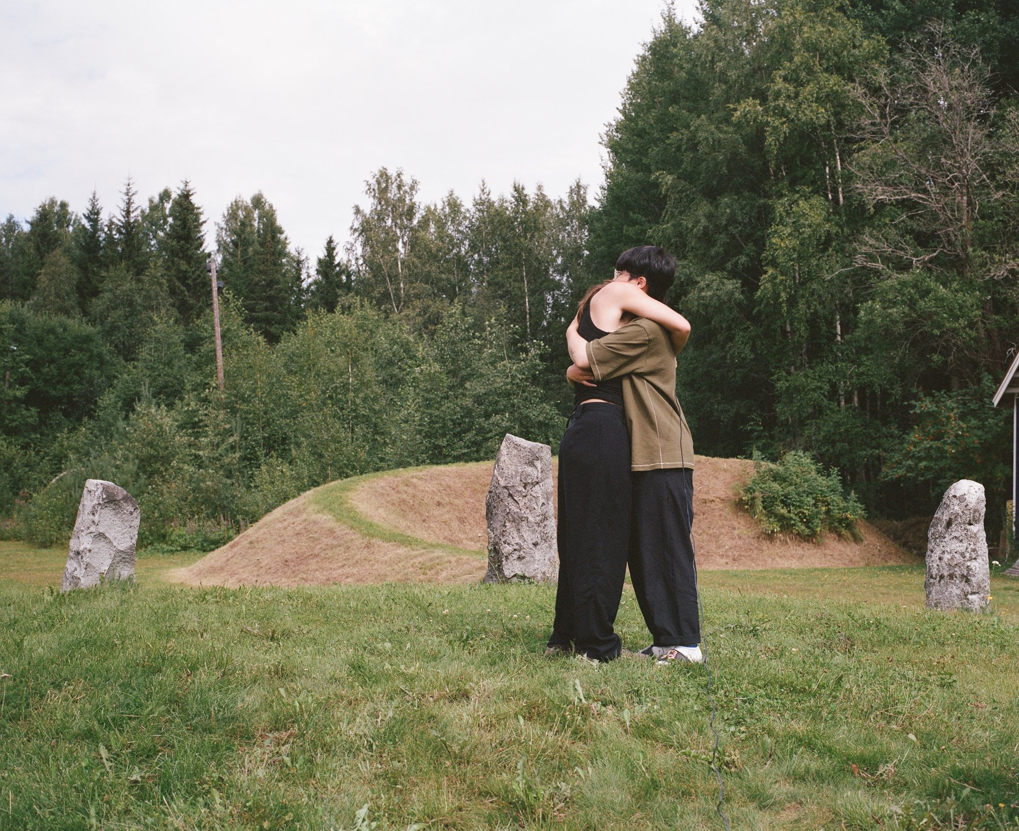Two figures embracing, seen from behind, among standing stones and a burial mound