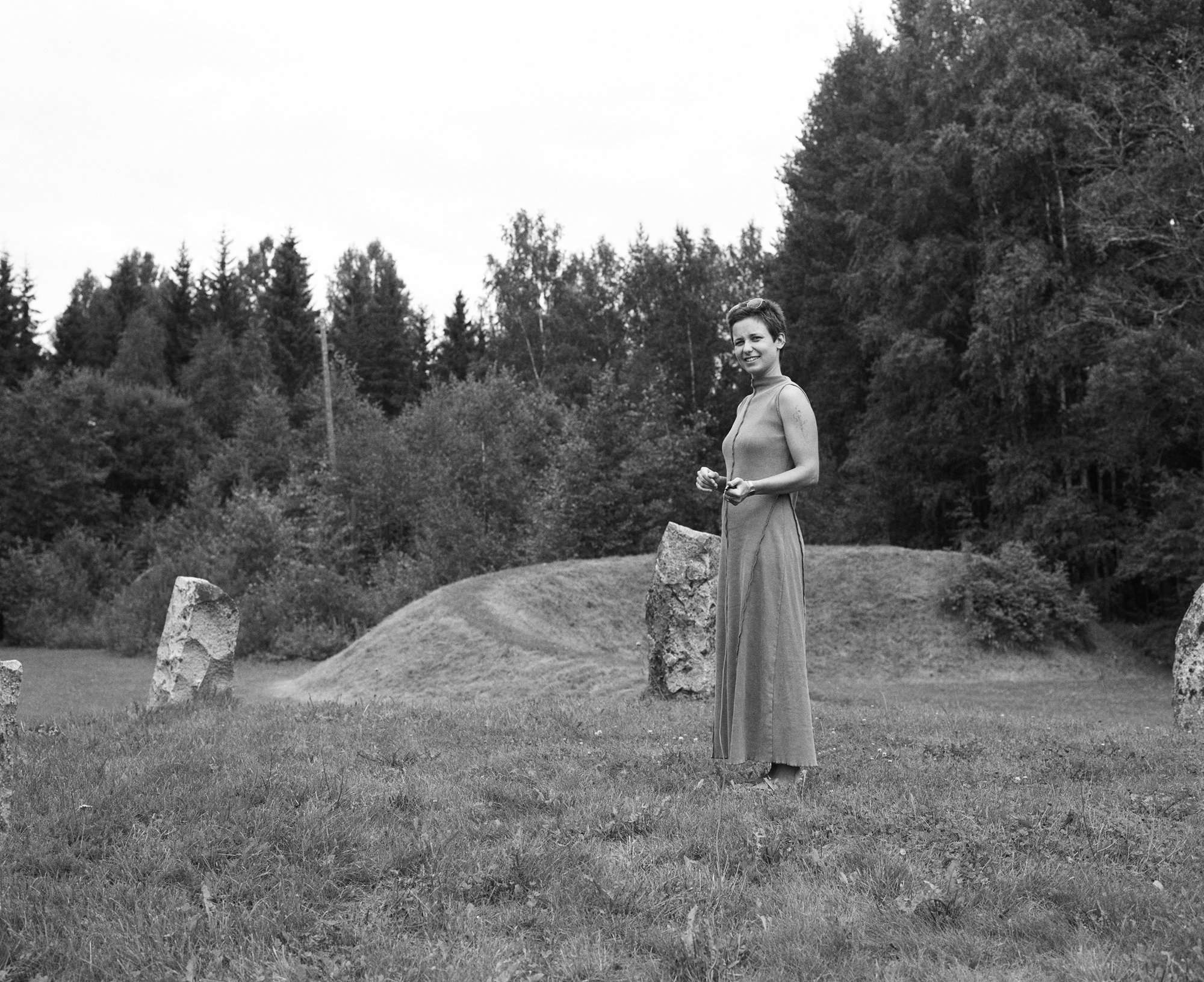 Black and white photograph of a woman standing among standing stones, smiling
