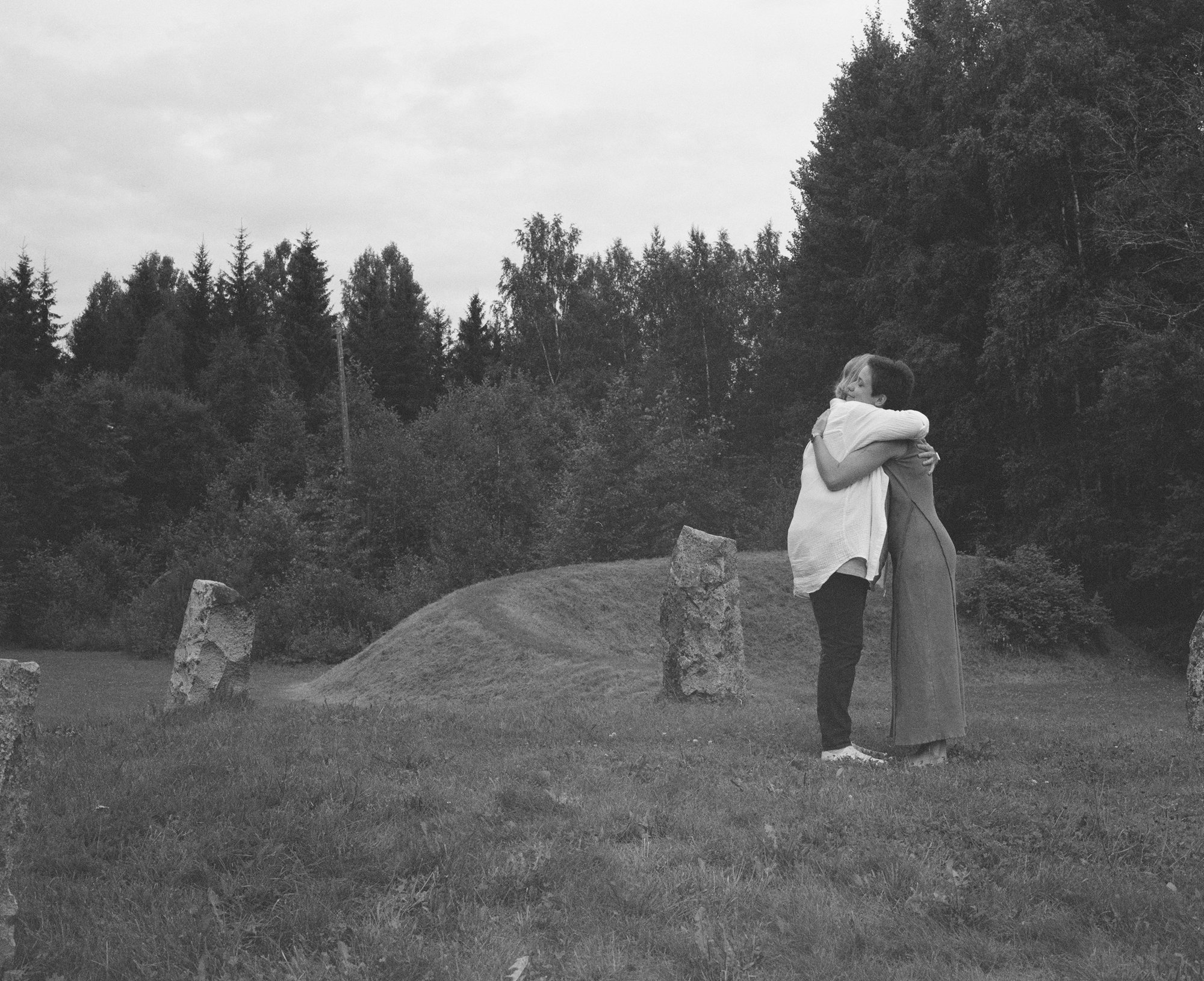 Black and white photograph of two figures embracing among standing stones