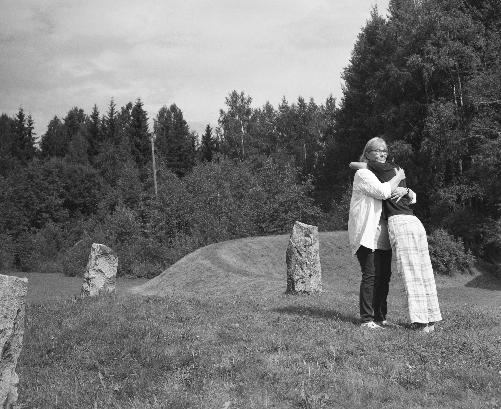 Black and white photograph of two figures embracing among standing stones