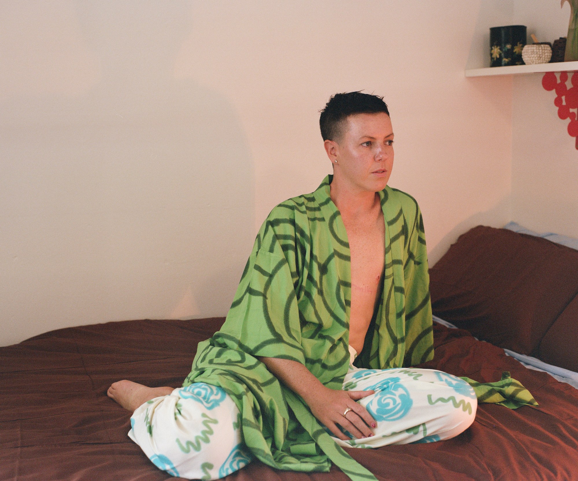 Portrait of a shirtless man sitting cross-legged on a bed with a patterned blanket