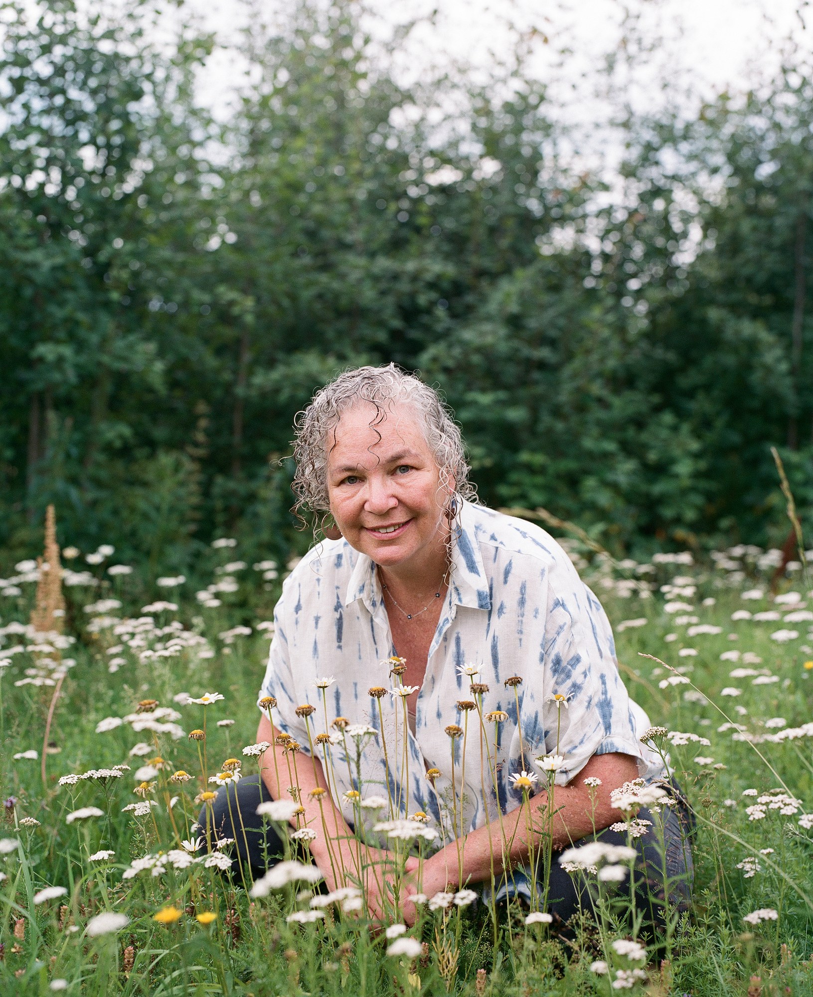 Portrait of an older woman kneeling in a field of daisies