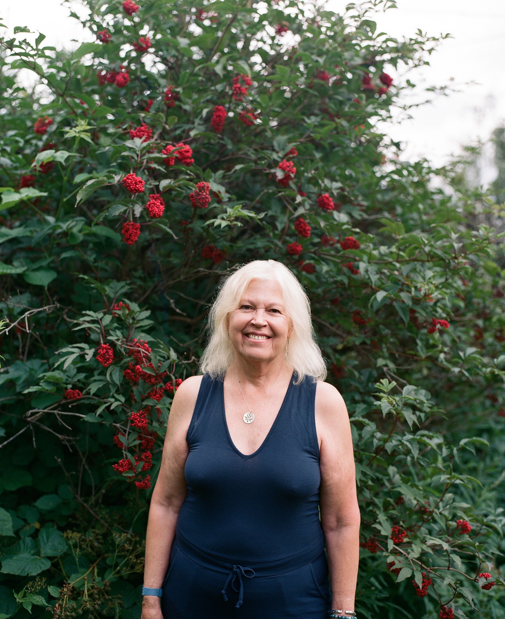 Portrait of an older woman smiling in front of a bush of red flowers