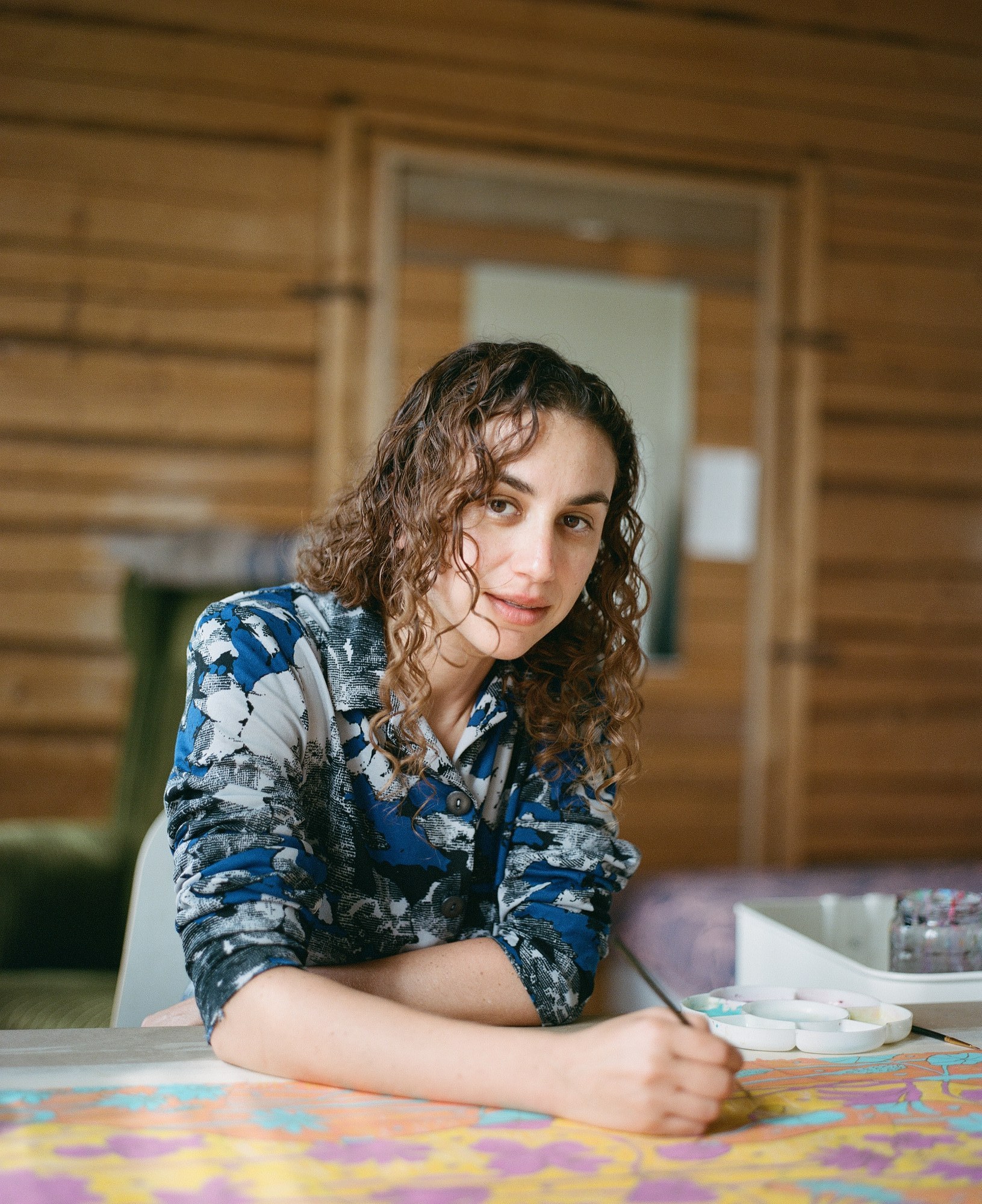 Portrait of a young woman leaning at a painting table, holding a paintbrush