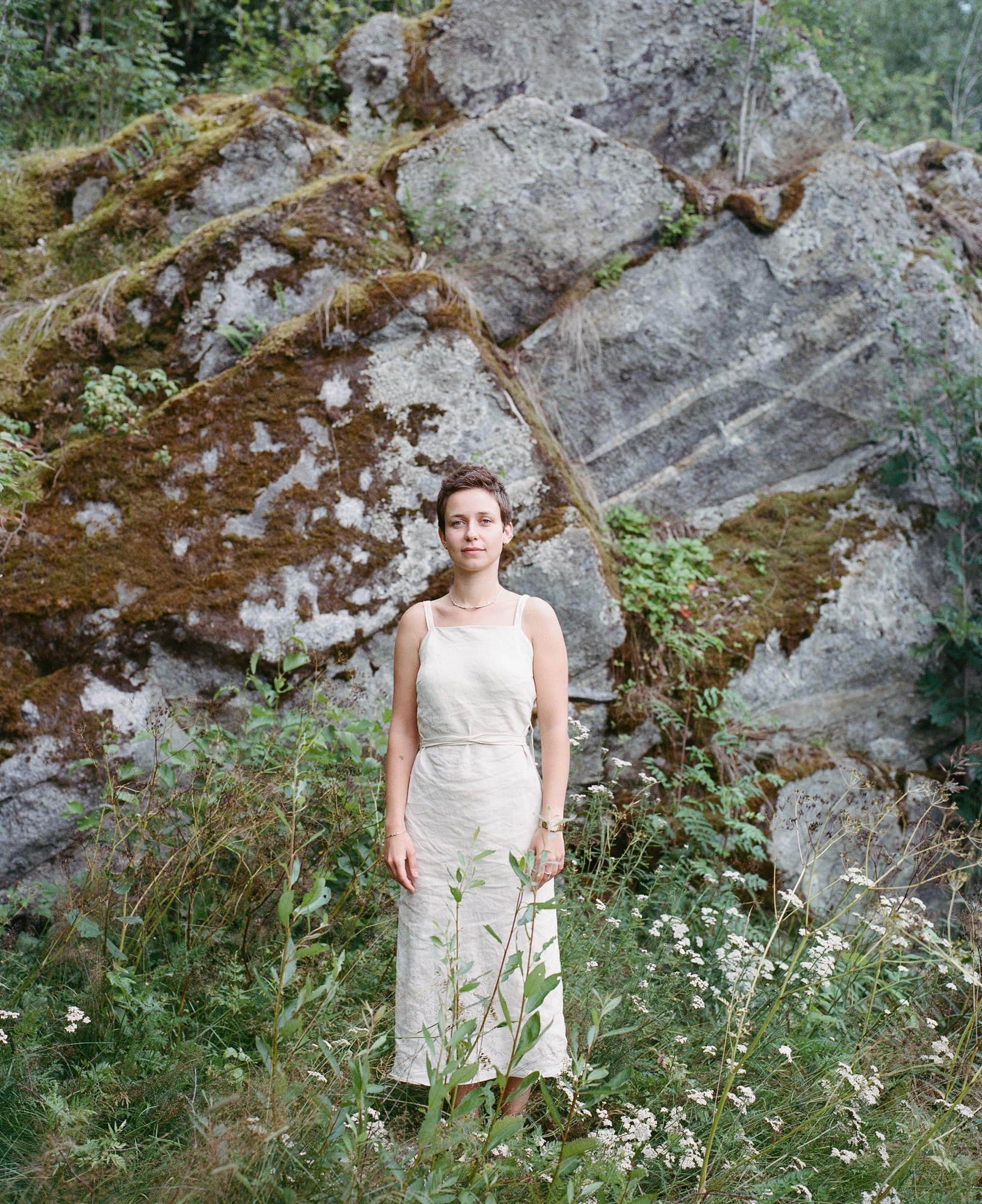 Portrait of a woman in a linen dress standing in front of a mossy rock