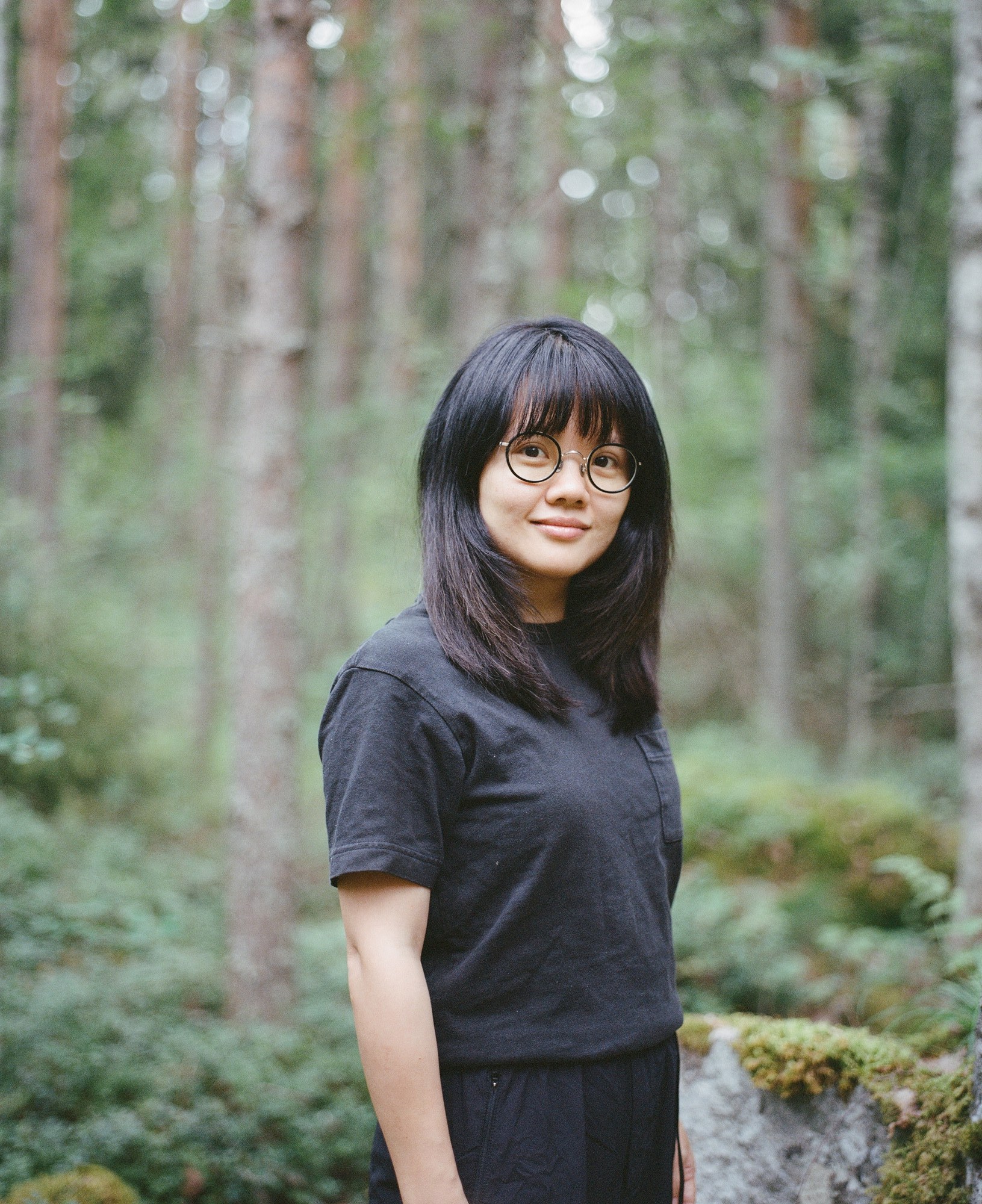 Portrait of a woman with round glasses smiling in a forest