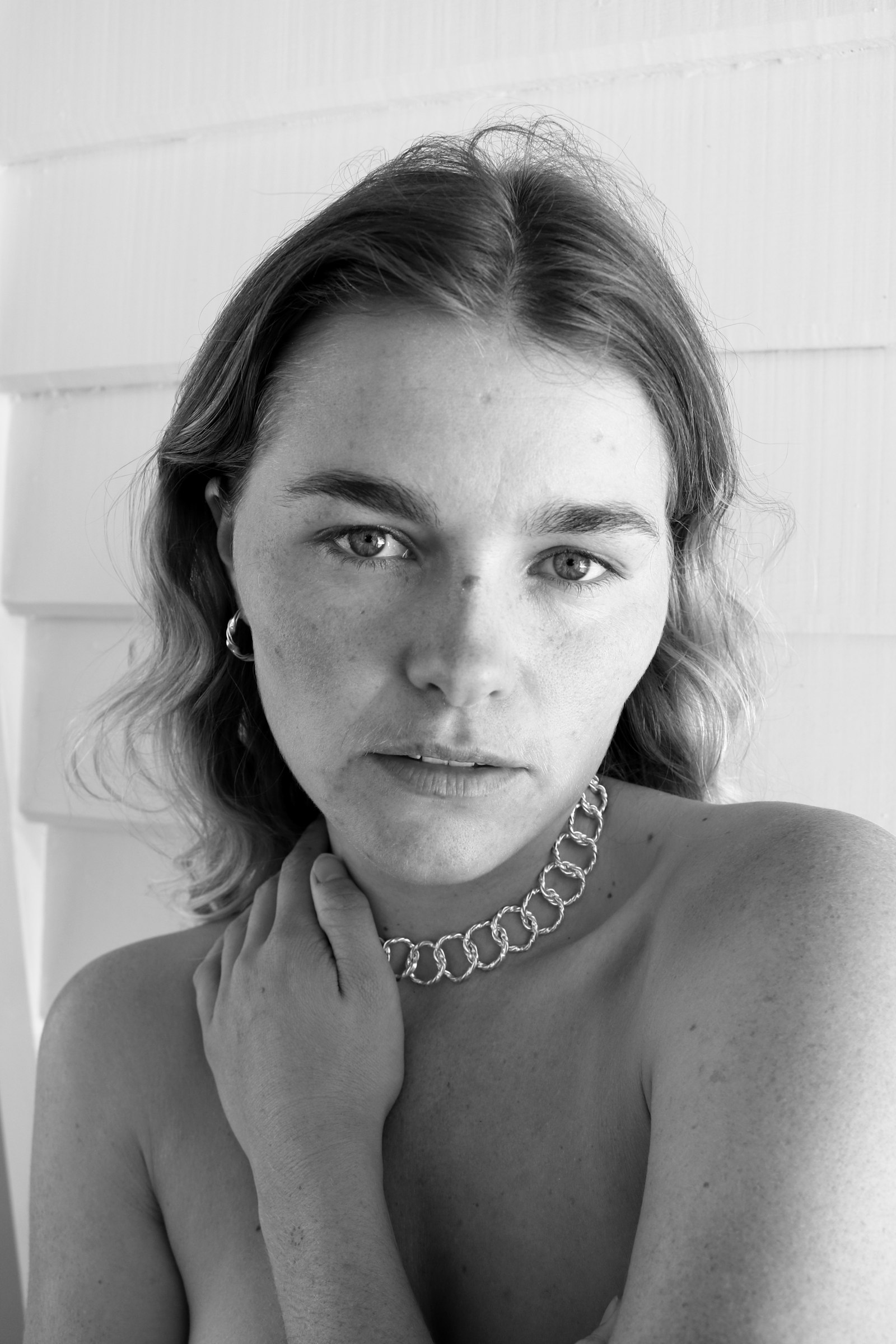 Close portrait of a woman wearing a chain necklace, hand resting at her collarbone