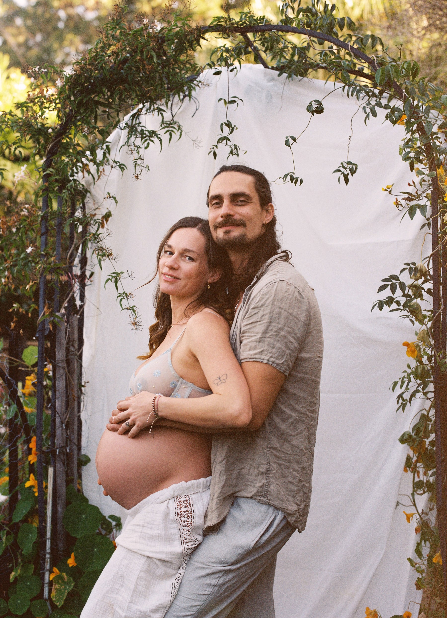 A pregnant woman and man embracing under a floral garden arch