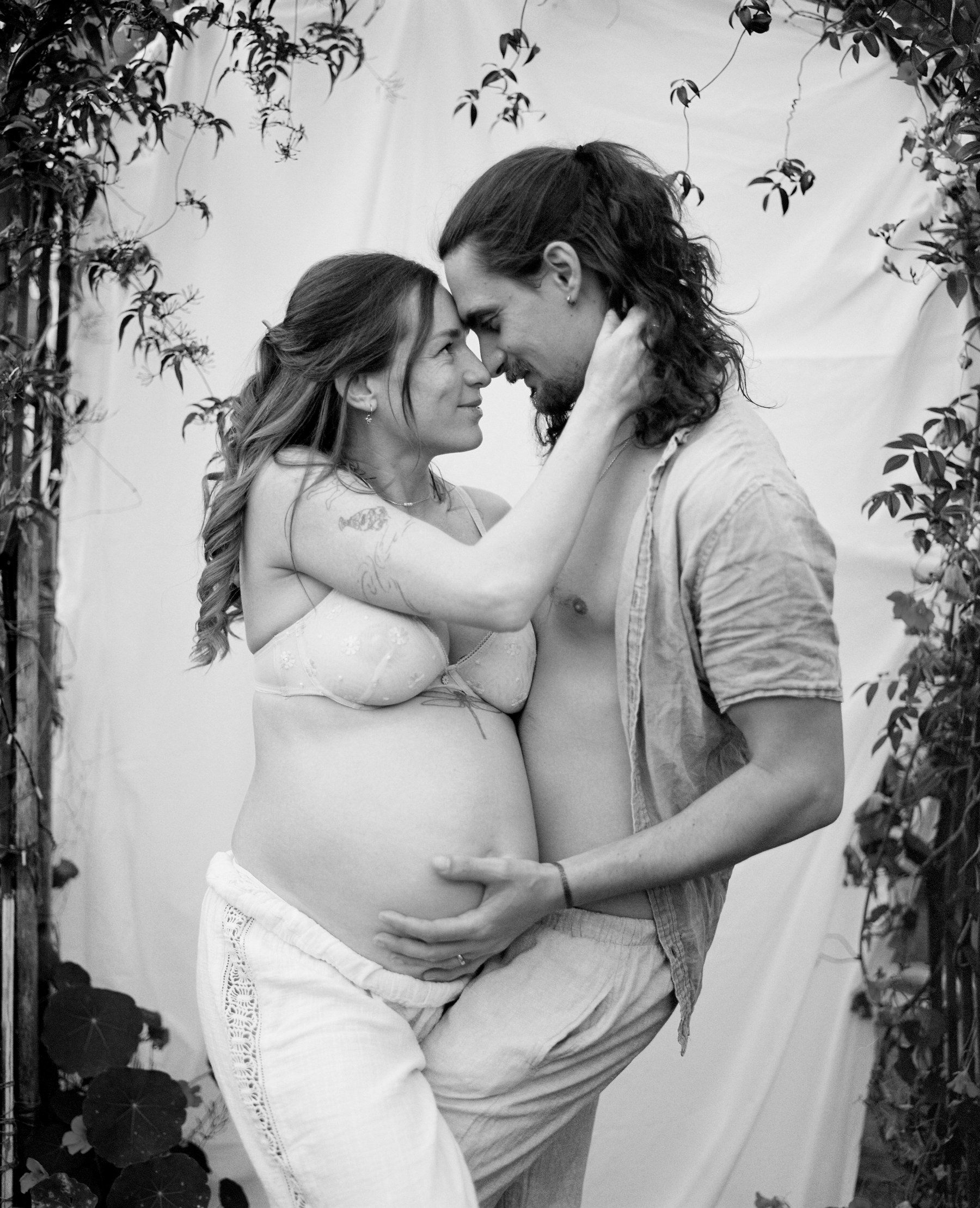 Black and white photograph of a pregnant woman and man embracing forehead to forehead