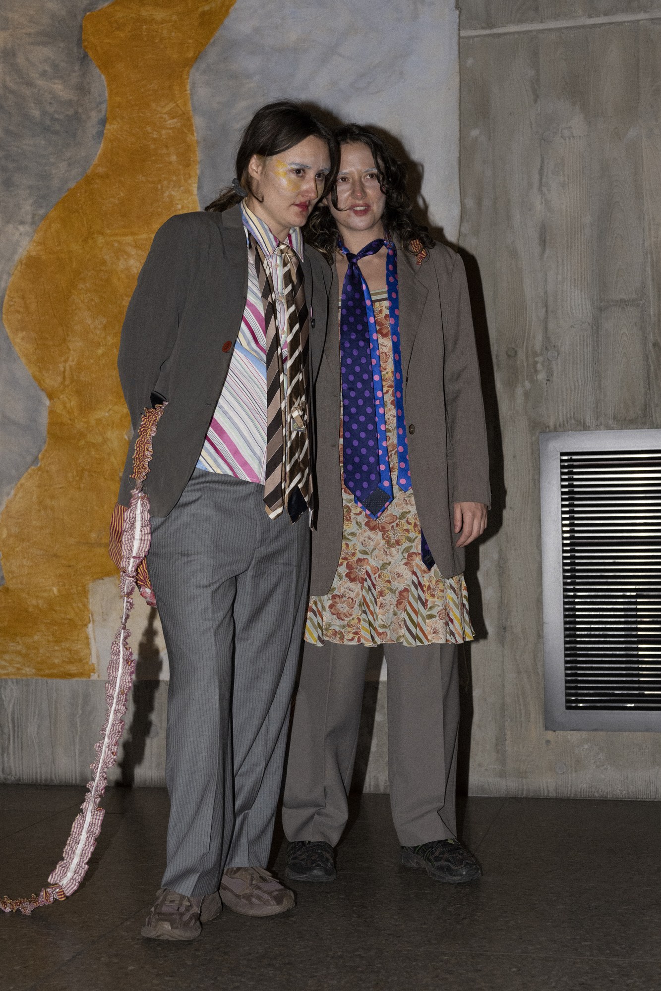 Two performers in grey suits with mismatched ties standing close together
