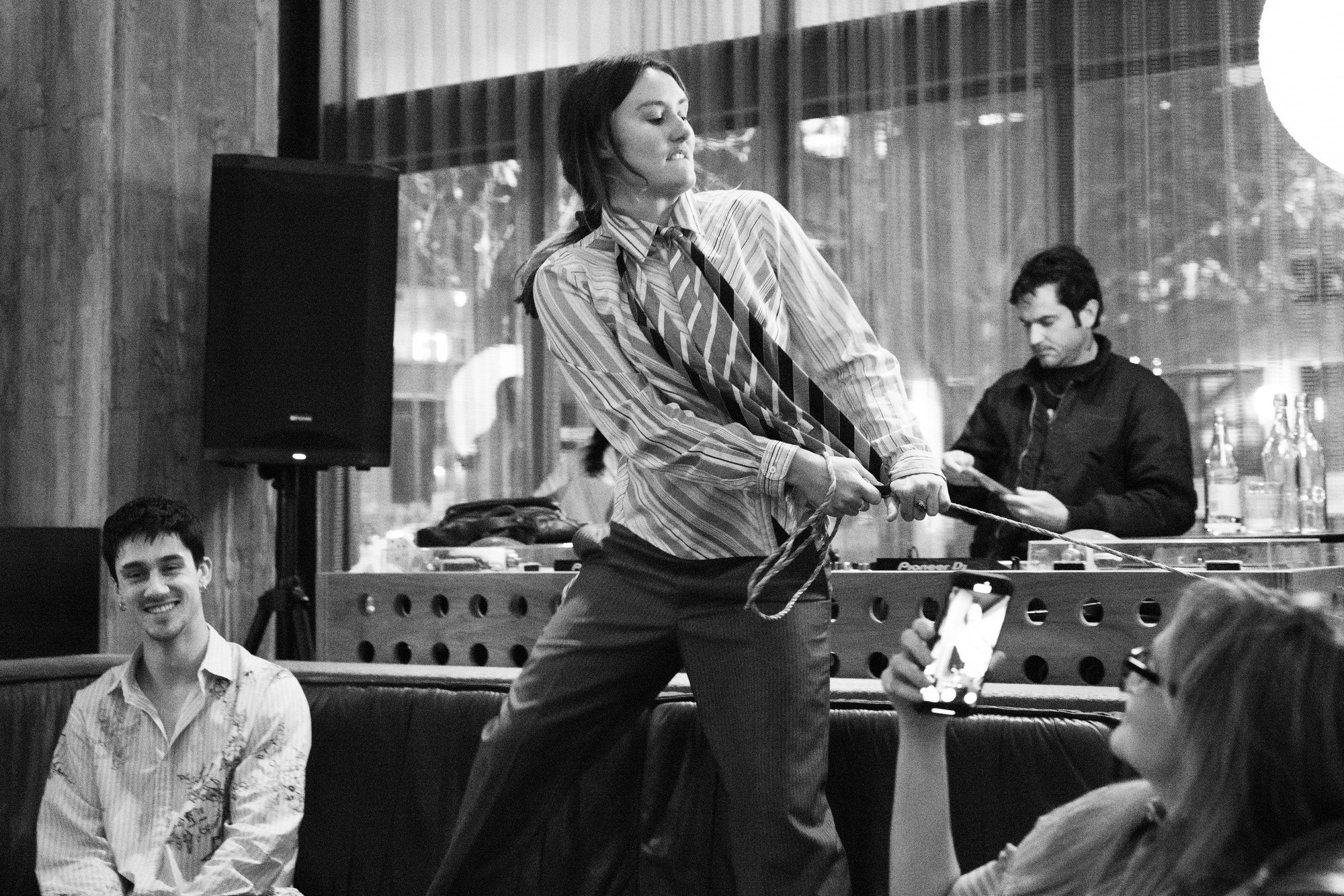 A performer seated as another hangs upside down from a table, a dollar bill pinned to a sleeve