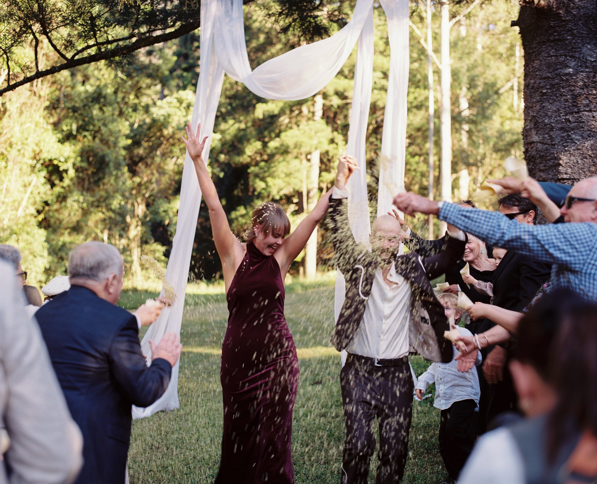 A bride and groom celebrating under white drapes as guests throw rice