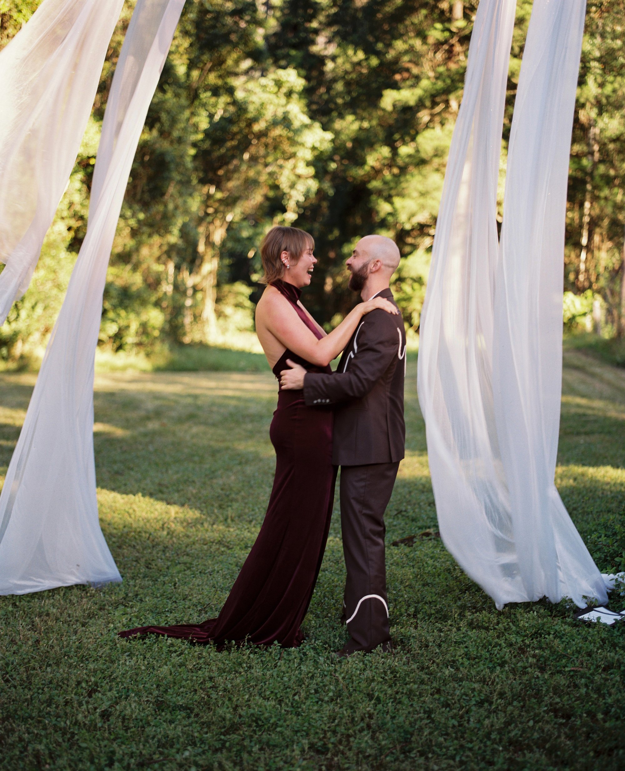 A bride and groom laughing and embracing under hanging white fabric