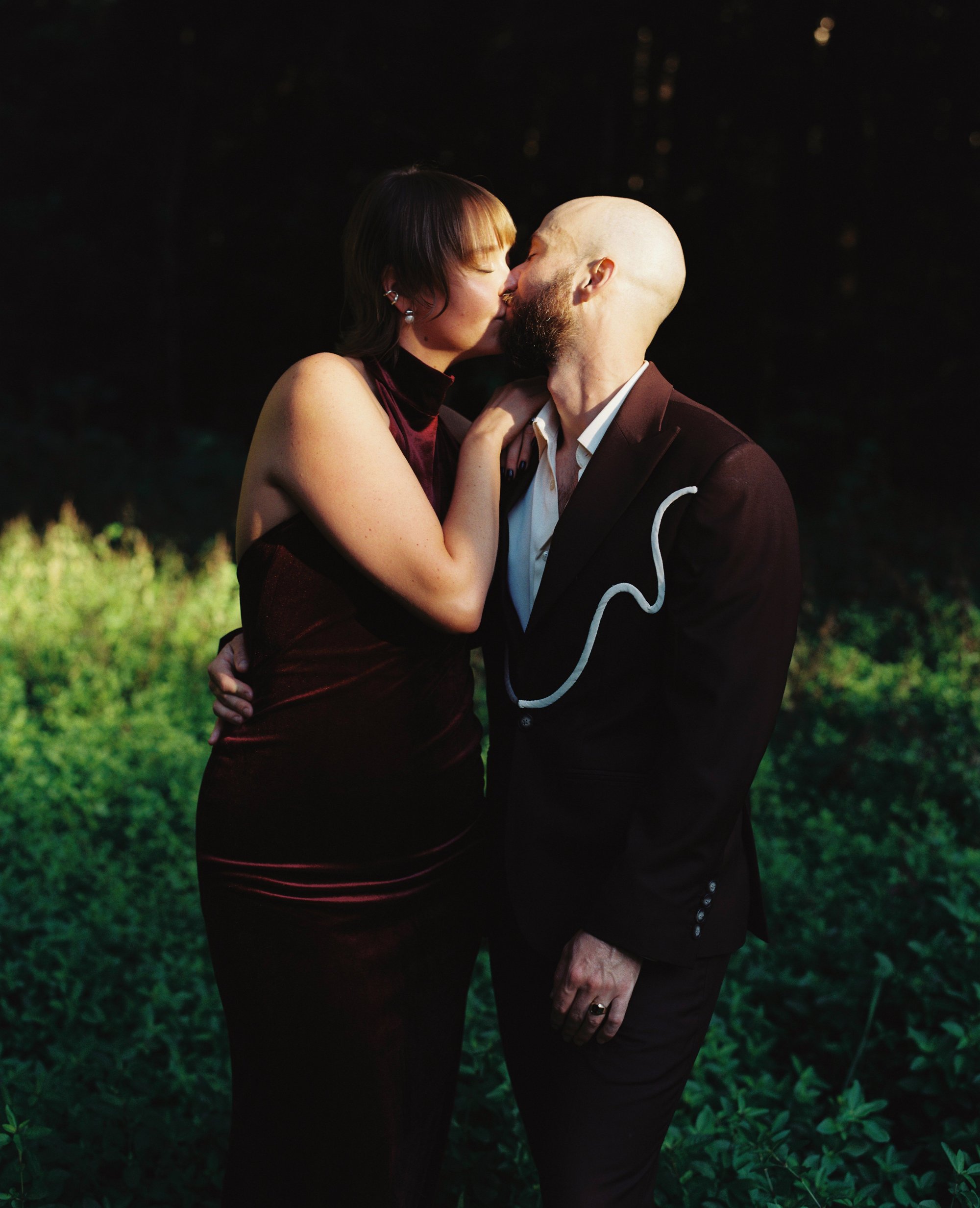 A bride and groom kissing in the shade of trees