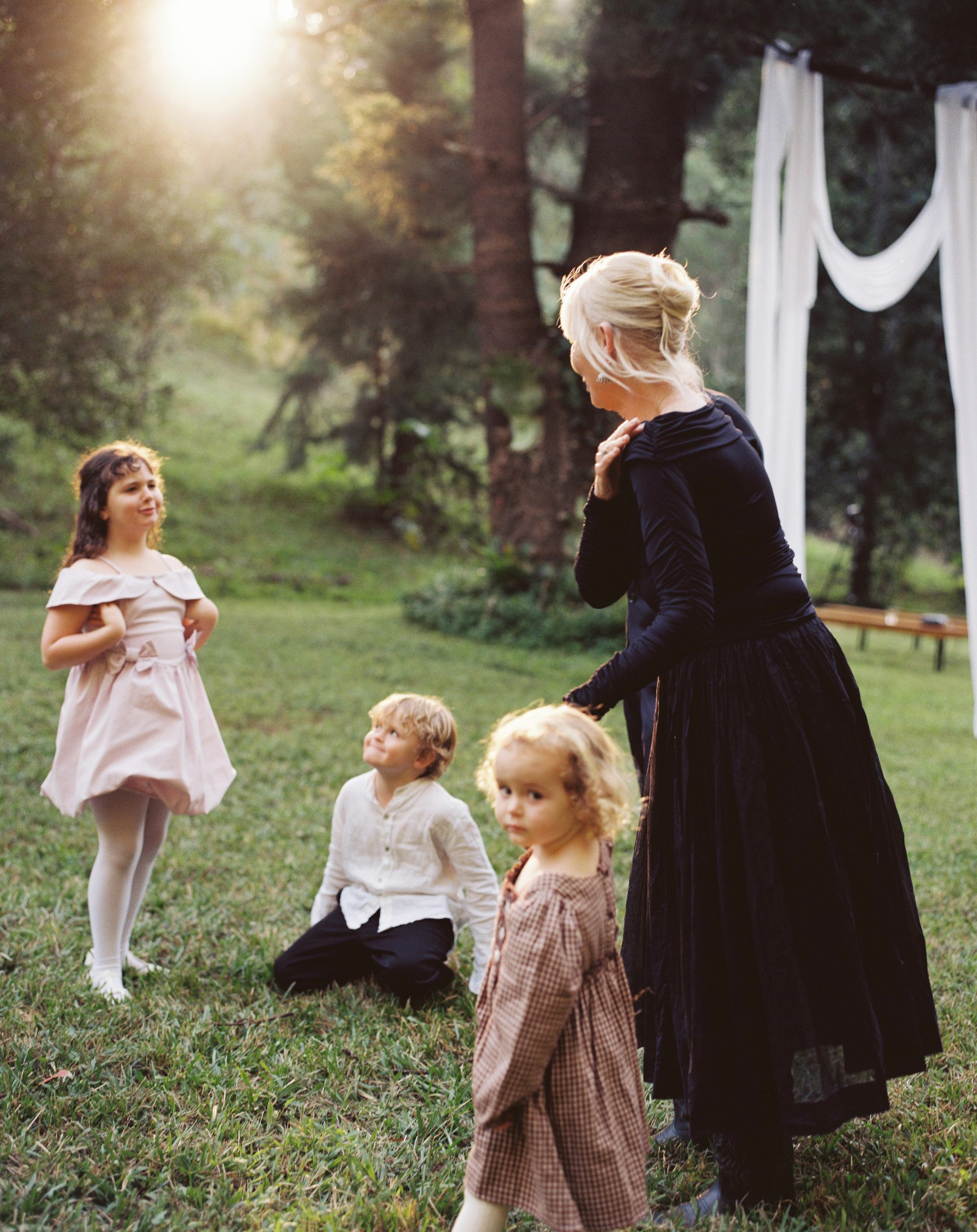 Children watching a woman in a navy dress adjust her shawl in a field