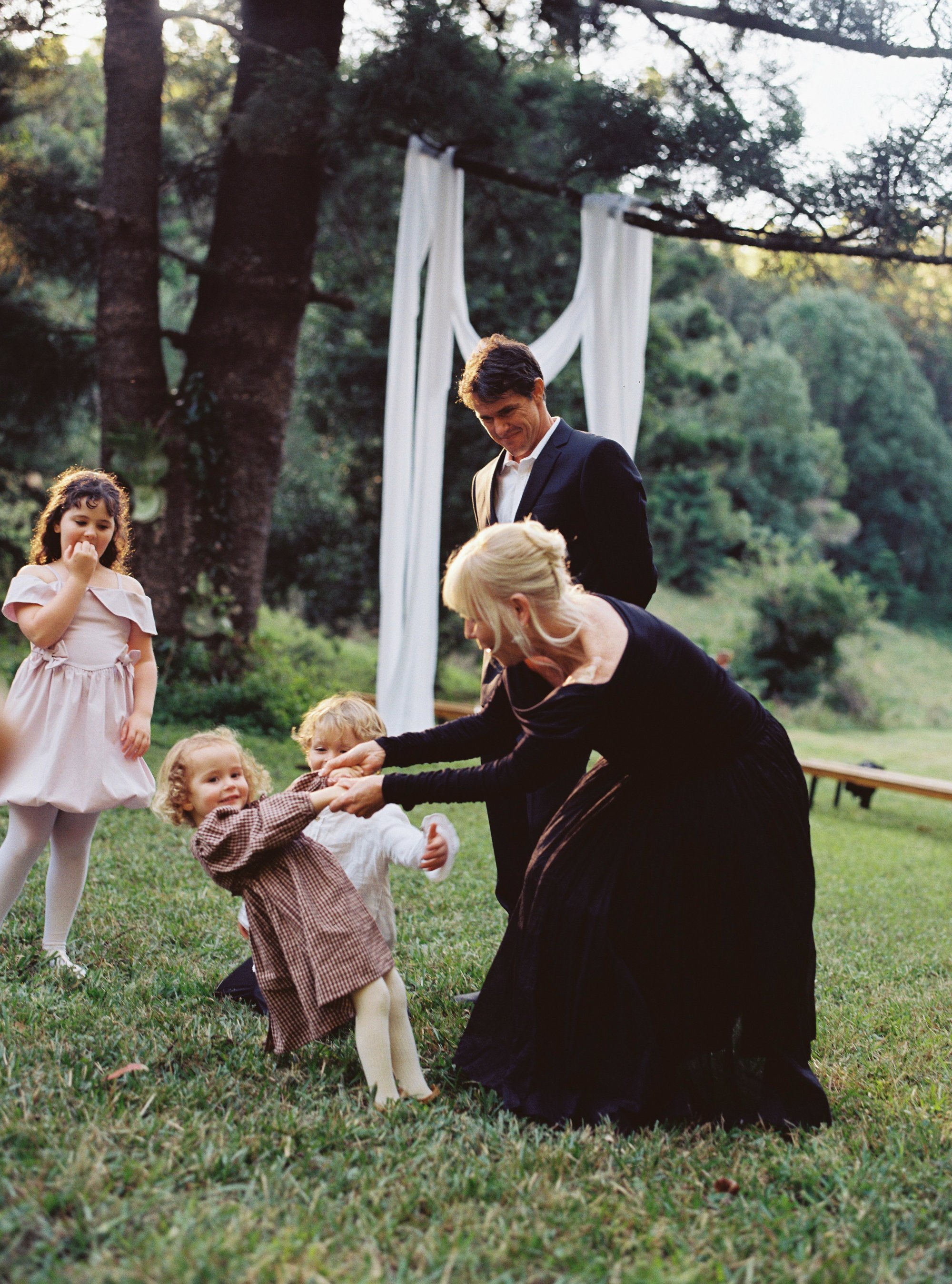 A woman dancing with young children in a field as a man looks on