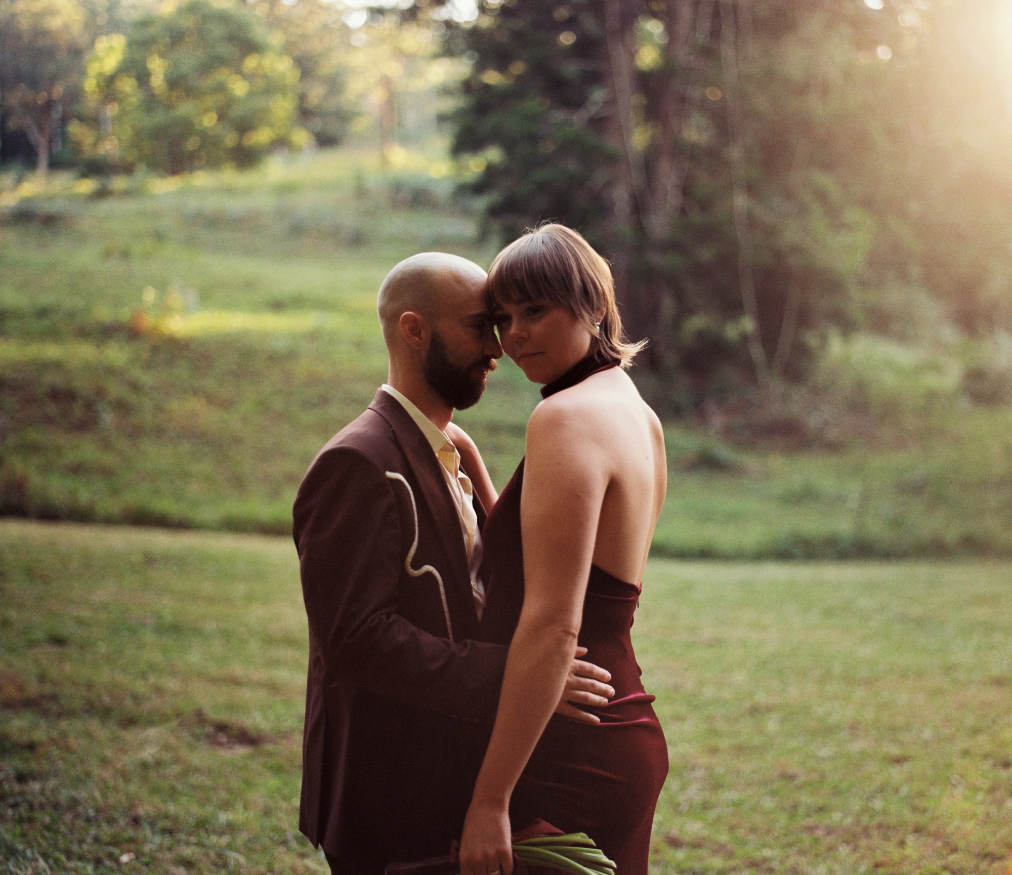 A bride and groom embracing in golden evening light in a field