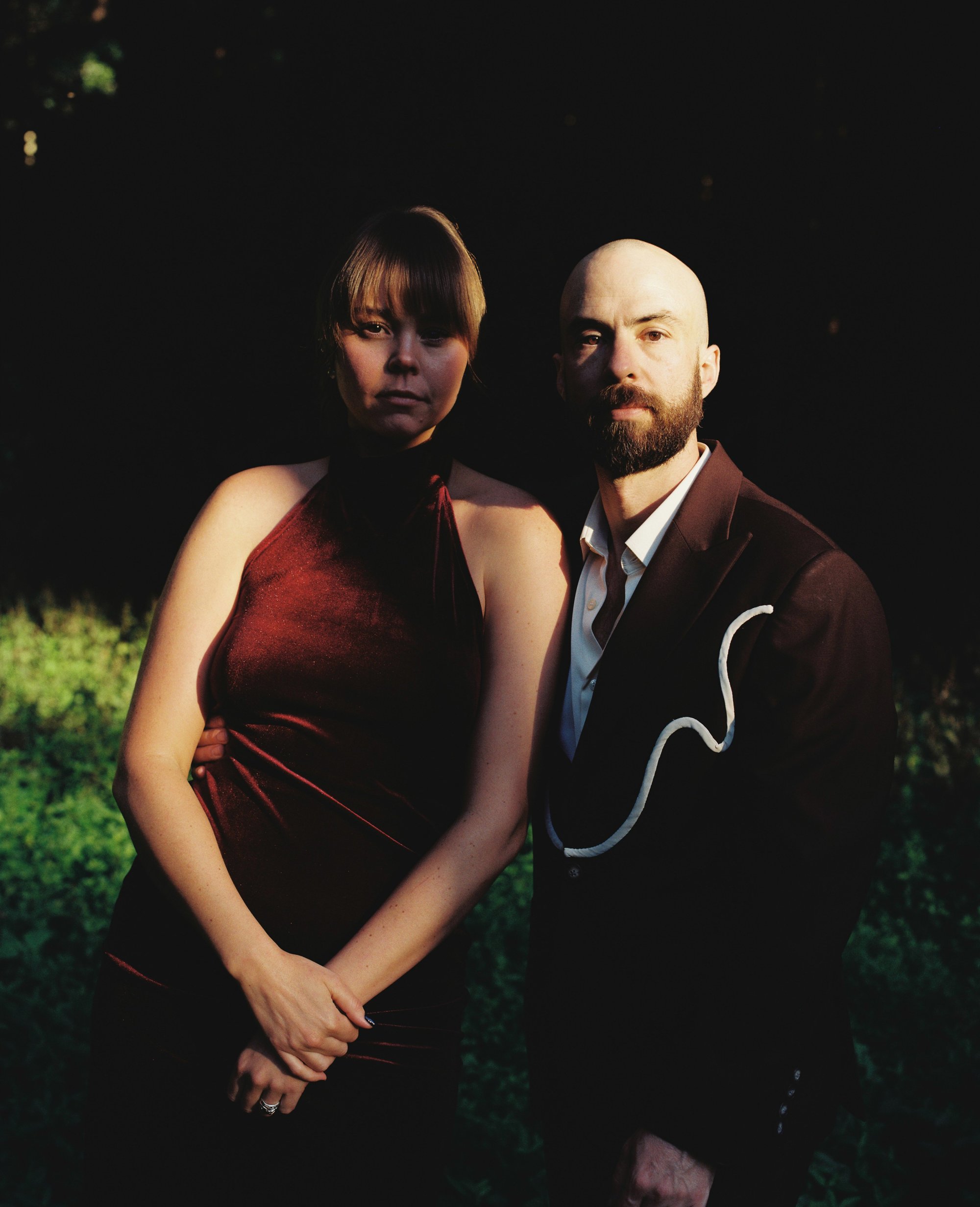 Portrait of a bride and groom lit by warm evening light against a dark background