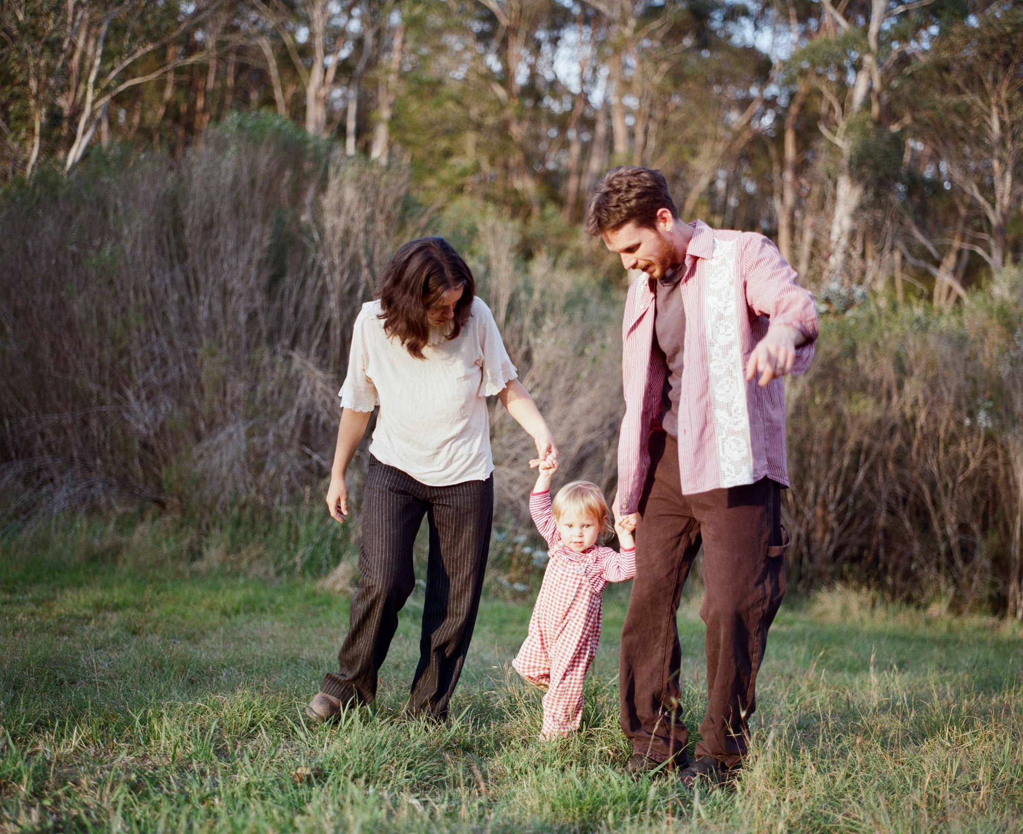 Parents walking a toddler by the hand through a field